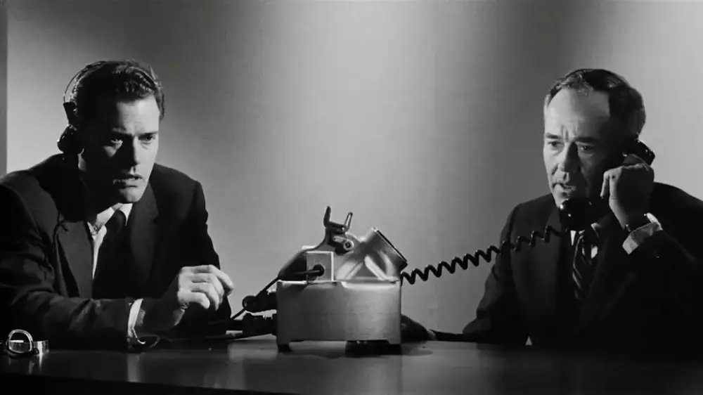 Två män sitter vid ett bord, och den ena av dem pratar i telefon.