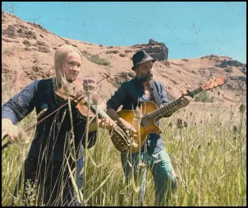 Fotografi av folkemusikerene Martine og Jørgen med fele og gitar utendørs i enga
