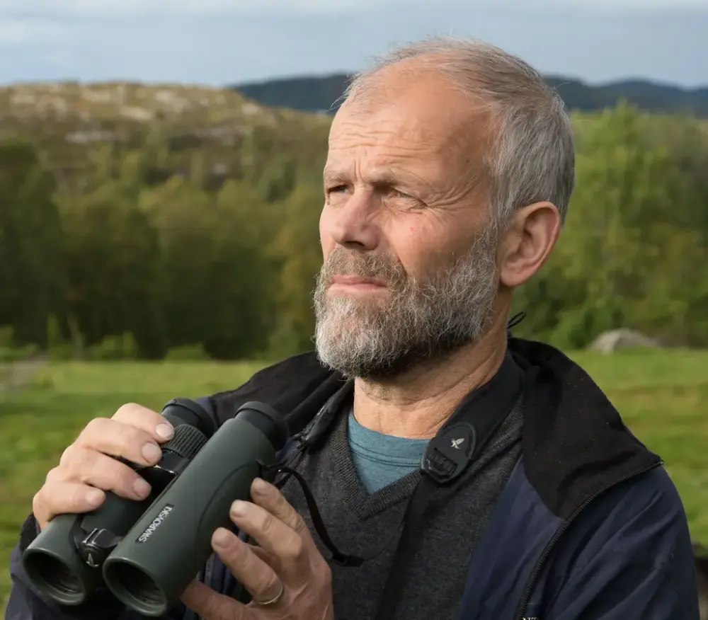 Portrett av Alv Ottar Folkestad ute i naturen med kikkert i hendene.