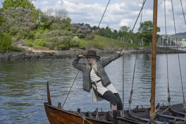 Kvinne henger i seilet på en båt og speider ut ovre havet. 