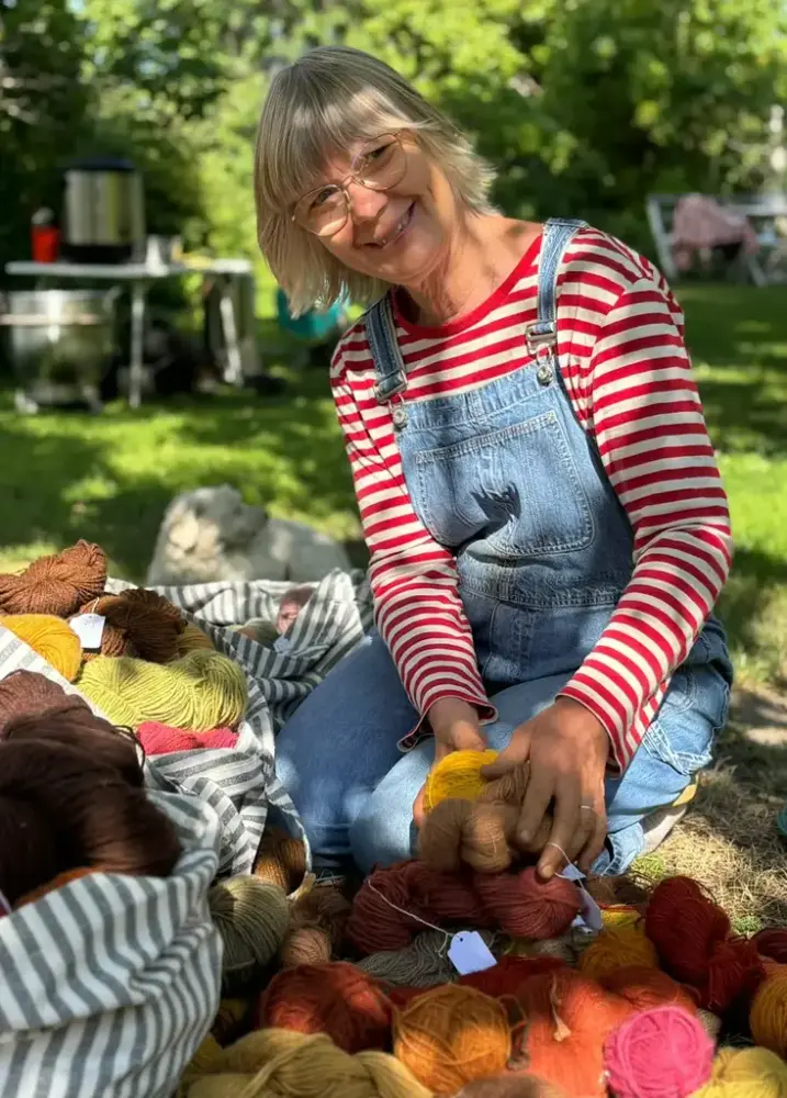 Mirjam i rödrandig tröja sitter i trädgården med garner som hon växtfärgat