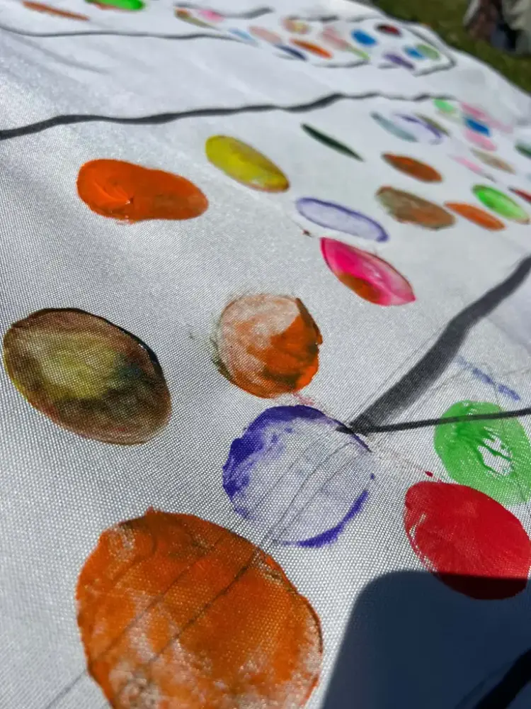 Hvitt, grovvevd tøystykke med striper og ujevne rundinger i ulike farger.