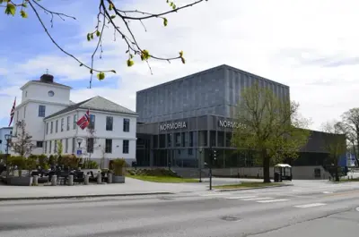 Nytt, kubeformet kulturhus i småby, med hvitt hus ved siden av og gate i forgrunnen