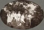 Ett sällskap med män, kvinnor och barn poserar för fotografen i en skogsglänta, en varm sommardag.
Trol. Amos Svensson med familj och vänner.