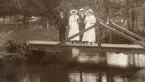Två herrar med damsällskap poserar på en liten träbro, en varm sommardag.