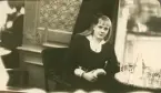 En tonårsflicka i mörk klänning sitter vid ett caféfbord.