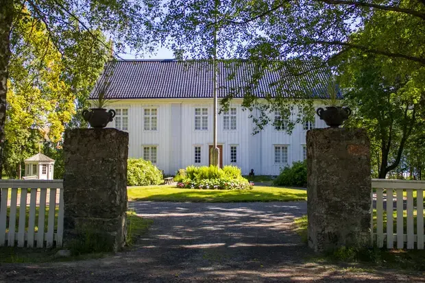 Åvike herrgård i solgasset, med grindstolparna med järnurnorna i förgrunden.