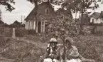 Två unga kvinnor vid ett litet äppelträd (?).