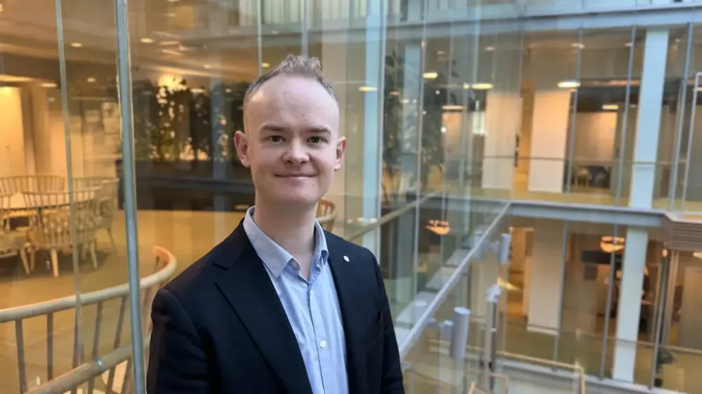 bildet viser en smilende mann foran en glassbygning. Det er av statssekretær Kristoffer André Hansen