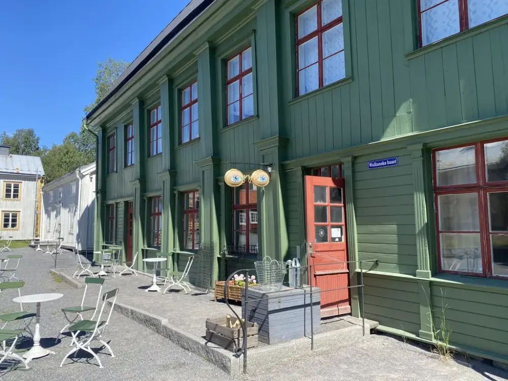Entrédörren står öppen till det gröna Wulkanska huset, med byggnadsvårds- och trädgårdsprylar utanför i solgasset.
