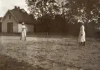 En tennismatch mellan systrarna Ruth och Blenda Svensson, trol. på skolgården till Östra Folkskolan, Alvesta. 
Till vänster syns en bod och bakom den skymtar ett bostadshus.