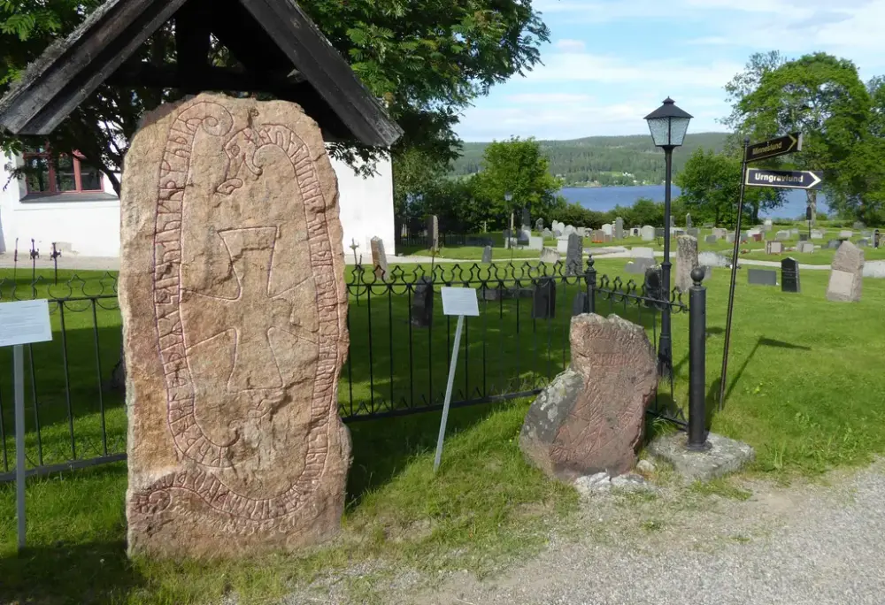 Två runstenar framför en kyrkogård och en vit kyrka.