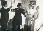 En utklädd Ruth Svensson i rock och hatt spelar fiol tillsammans med några roade vänner.
Kvinnan till höger slår takten med några grytlock.