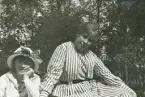Två unga kvinnor i rutiga och randiga sommarklänningar m.m. tittar tankfullt mot fotografen.
Kvinnan till vänster - Ruth Svensson.