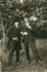 En man och en ung kvinna (utklädd till man i kostym och hög hatt) poserar för fotografen i en trädgård.
Kvinnan är Ruth Svensson.