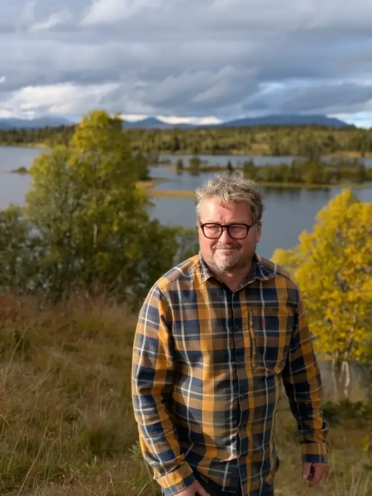 Mann med rutete skjorte i skog- og sjølandskap