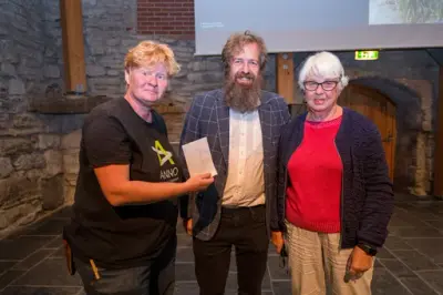 F.v. Hildur Hauksdottir (leder i Urtehagen på Domkirkeodden), avdelingsdirektø Per Øyvind Riise og leder for Domkirkeoddens venner, Ingrid Hatlemark. De var samlet i Aulaen i forbindelse med Urtehagens 50-årsjubileum i 2025, og venneforeningen donerte penger.