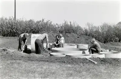 Svart-hvitt fotografi av medlemmer av Domkirkeoddens venner da de bidro til å legge opp murringer til blolmsterbed i forbindelse med opprettelsen av Urtehagen på Domkirkeodden midt på 1970-tallet.