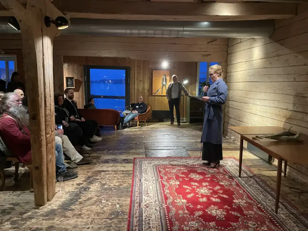 Vi ser riksantikvar Heidi Geiran stå foran en liten forsamling under åpningen av tørrfiskutstillingen på Norges Fiskerimuseum
