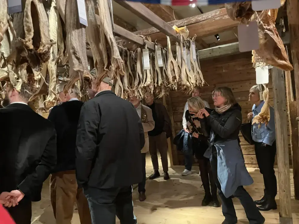 Vi er i en gammel sjøbod, det henger tørrfisk fra taket og folk står og ser på