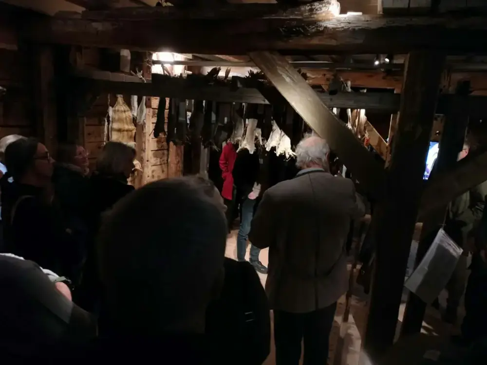 Vi er i en gammel sjøbod, det henger tørrfisk fra taket og folk står og ser på
