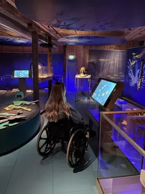 Her ser vi en jente i rullestol som sitter og leser på monitoren i utstillingen verden under vann