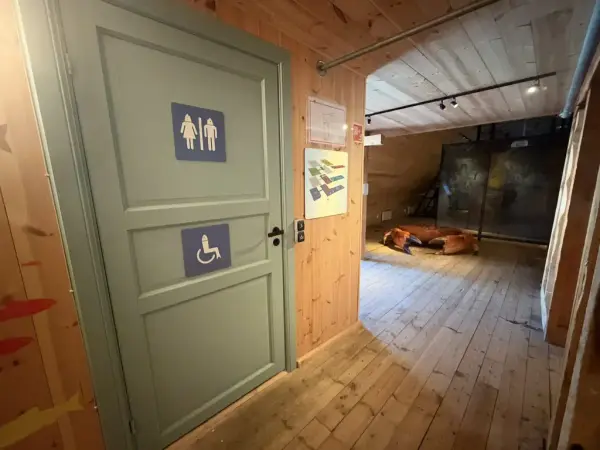 Vi ser døren til toalett i utstillingen Det eventyrlige fisket, like ved den store krabben Oluf. 