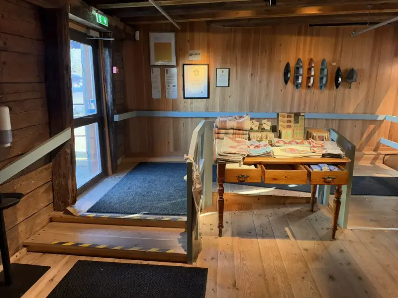 BIldet viset inngangspartiet i museet, døren går utover, det er en liten terskel å komme over før en kommer inn. Inn til venstre er rullestolrampen, mens det til høyre er to trinn ned. 