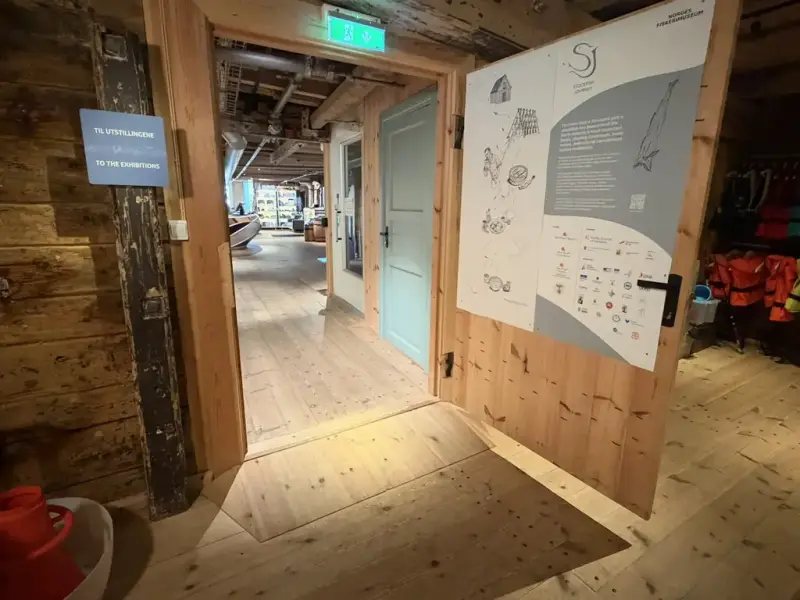 Vi ser en stor dør som står åpen og videre inn i resepsjonen ved museet. I døråpningen er det en liten rampe slik at det er tilrettelagt for barnevogner og rullestoler. 