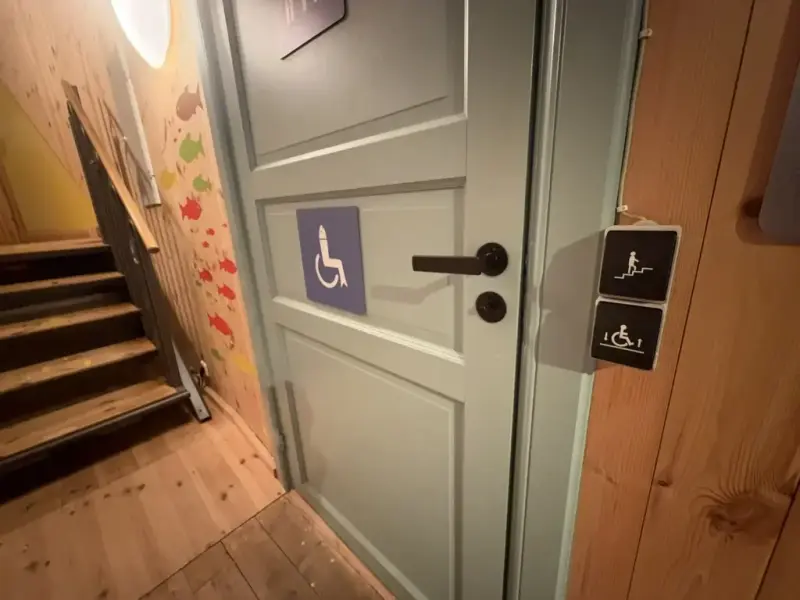 Bildet viser litt av trappeheisen, døren inn til toalettene og knappene som brukes for å gjøre trappene om til en rullestolheis