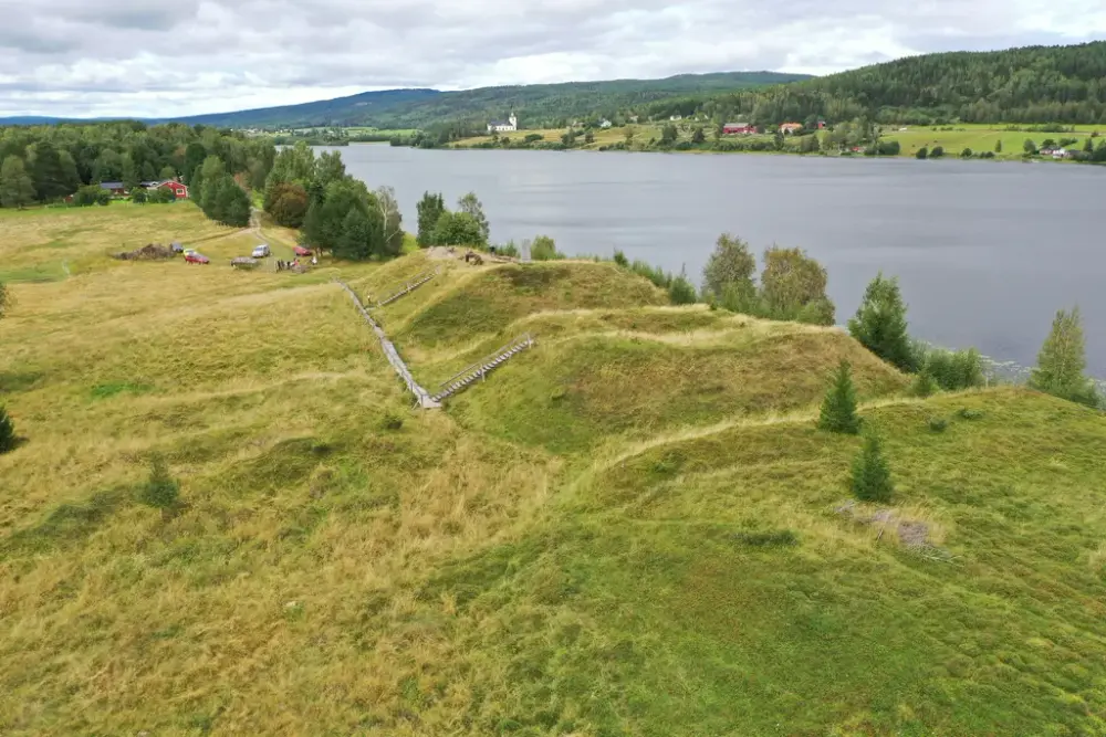 Landskap med gräsbeklädda kullar, skog och älv.